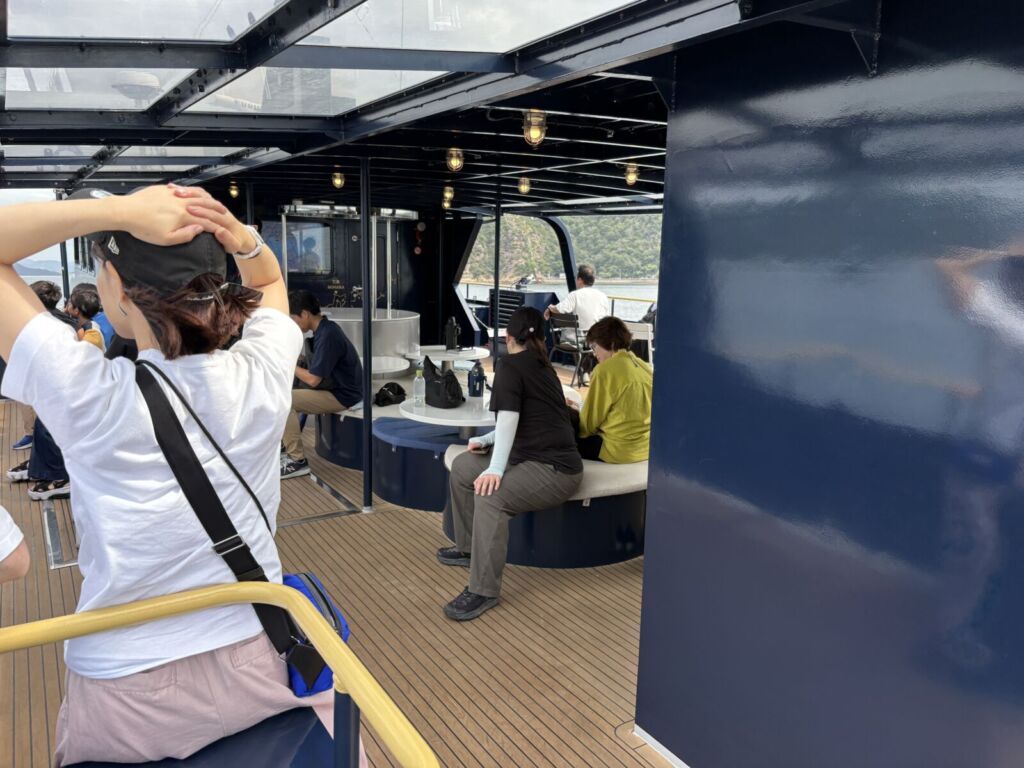 SEA SPICAの2階オープンデッキ。丸テーブルとベンチに乗客が腰かけ、奥に瀬戸内の島影が見える