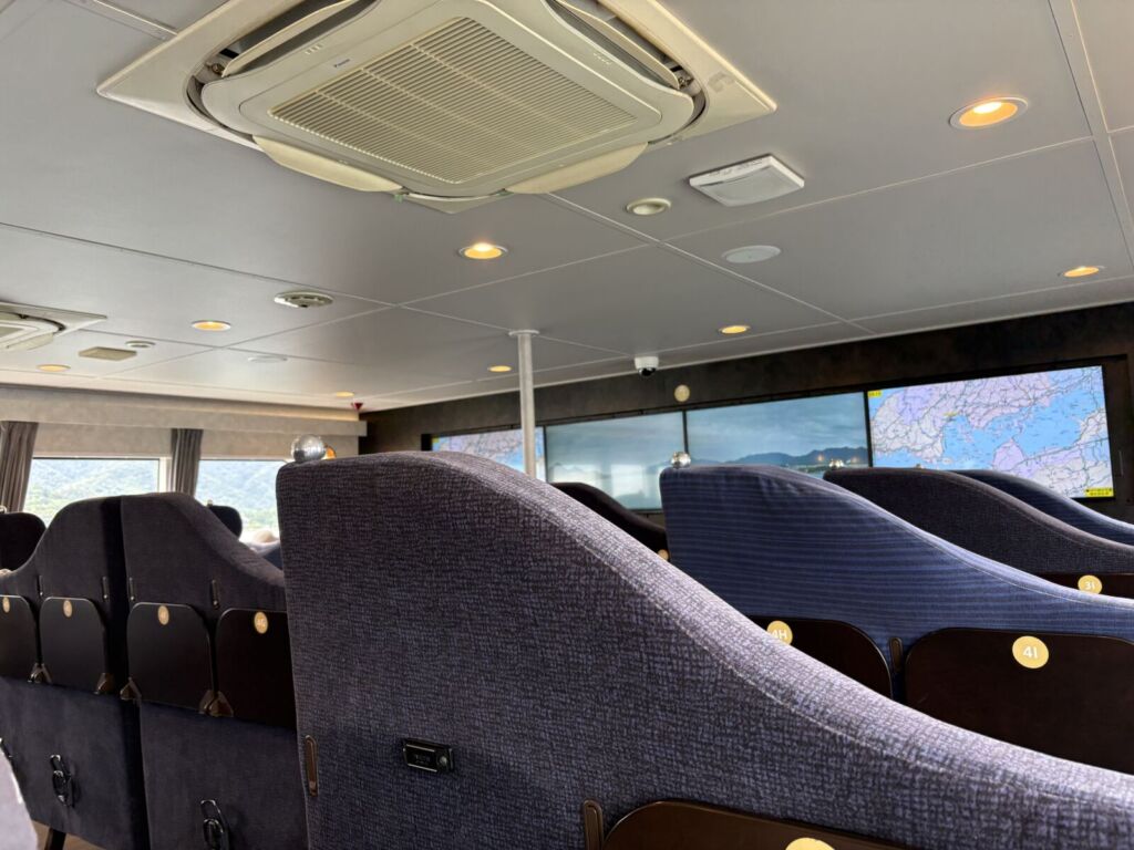 高速クルーザーSEA SPICAの客室。濃紺の3人がけシートが並び、前方に航路案内のモニターが設置されている