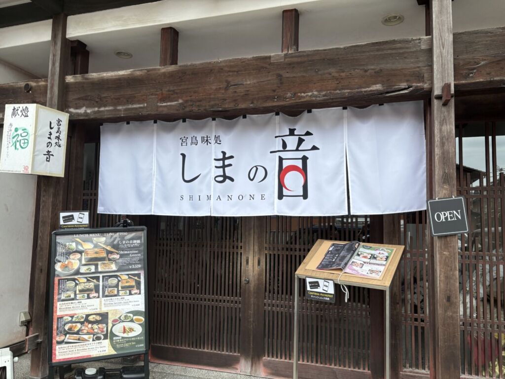 宮島味処しまの音の外観。白い暖簾に店名が染め抜かれ、店頭にランチメニューの看板が立てられている