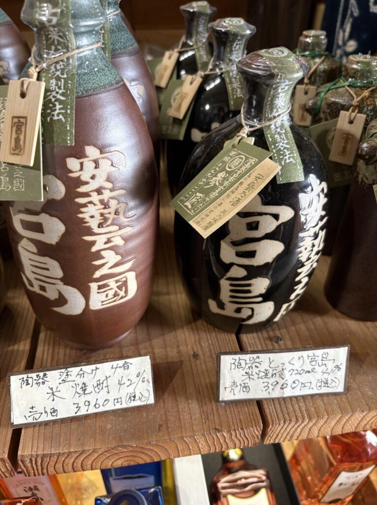 宮島の酒屋に並ぶ陶器製ボトルの米焼酎。「安藝之國 宮島」の文字が入り、値札に「陶器 とっくり宮島 米焼酎 720ml 41%」とある