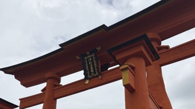 見上げた厳島神社の大鳥居。反り返った黒い屋根の下に「伊都岐島神社」の扁額が掲げられ、朱塗りの柱が空に伸びている