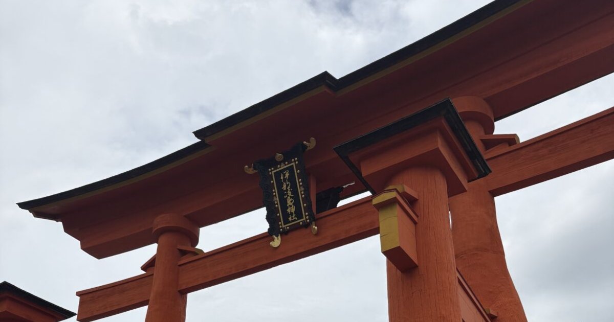 見上げた厳島神社の大鳥居。反り返った黒い屋根の下に「伊都岐島神社」の扁額が掲げられ、朱塗りの柱が空に伸びている